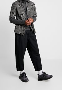 Chemise à manches courtes avec un motif floral noir et blanc, associée à un pantalon sombre ample et des baskets noires texturées.
