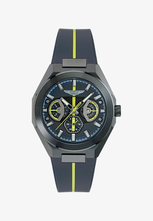 Montre analogique noire et grise avec des accents jaunes, trois sous-cadrans affichant le jour, la date et l'heure sur 24 heures, et un bracelet noir avec une bande jaune.