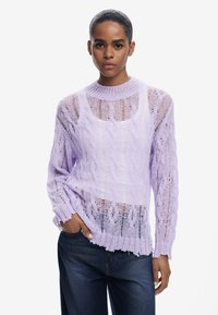 Lila gestrickter Pullover mit Lochmuster, Rundhalsausschnitt, langen �Ärmeln und ausgefranstem Saum. Kombiniert mit dunklen Denim-Jeans.