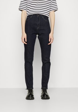 Jeans de ganga escuros de cintura alta, com um corte slim, apresentando cinco bolsos e costuras clássicas, combinados com uma camiseta às riscas em preto e branco.