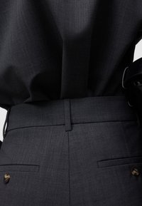 Donkergrijze op maat gemaakte broek met een gladde textuur, voorzien van een platte tailleband, twee achterzakken met knoopsluitingen en een subtiel geweven patroon.