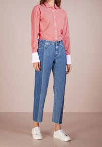 Röd- och vitrandig långärmad skjorta med vita manschetter, matchad med ljusblå denim raka jeans med fransade kanter och vita sneakers.