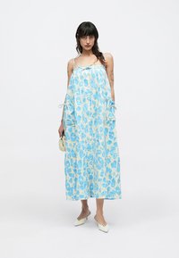 Μακρύ φόρεμα με μοτίβο σε μπλε και κρεμ αποχρώσεις, με φαρδιά εφαρμογή, λεπτές τιράντες και δεσίματα στα πλαινά. Συνδυάζεται με παπούτσια ανοιχτού χρώματος.