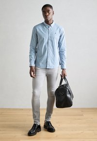 Light blue checkered button-up shirt, gray slim-fit jeans, black leather shoes, and a black leather bag with rounded shape and dual handles.
