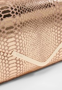 Kabelka ve tvaru psaníčka v růžově zlaté barvě s texturovaným vzorem hadí kůže, zdobená zlatým akcentem. Hladký povrch s metalickým leskem.