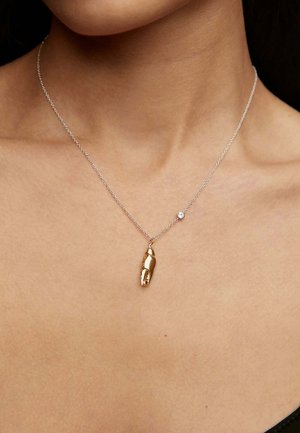 Collar de oro en forma de mano, unido a una delgada cadena de plata, con un pequeño acento de gema clara cerca del broche.