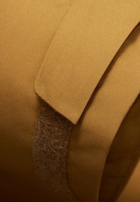 Gros plan sur un tissu marron avec une sangle texturée et duveteuse. Présente une finition lisse et mate ainsi qu'un design à rabat.