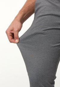 Gray, stretchy athletic pants with a textured finish; hand gripping the fabric near the thigh, showing flexibility and fit.