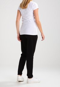 Bílý přiléhavý tričko s krátkým rukávem, spárované s černými zúženými joggery. Model má na sobě bílé sportovní tenisky. Hladká tkanina, minimalistický design.