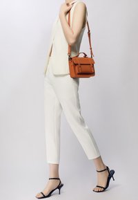 Biały dopasowany kamizelka i spodnie, w zestawieniu z czarnymi sandałami na wysokim obcasie. Mała pomarańczowa skórzana torebka z uchwytem na górze i paskiem na ramię.