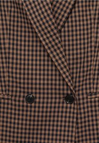 Blazer à carreaux marron et noir avec revers, deux boutons noirs et deux poches passepoilées.