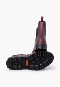Bottines bordeaux avec semelles en caoutchouc noir, présentant une texture antidérapante, des panneaux élastiques sur les côtés et une languette à l'arrière.