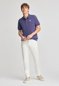 Lila pikétröja med krage och korta ärmar, kombinerad med vita slim-fit byxor och beige sneakers. Har en liten logotyp på bröstet.