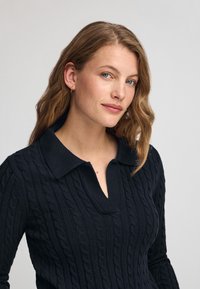 Granatowy pulower z dzianiny w warkocze z kołnierzykiem i zamkiem na ćwierć. Posiada fakturowany wzór i długie rękawy.