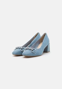 Chaussures à talons hauts en denim bleu avec un bout pointu, ornées d'une chaîne en argent et d'un talon bloc carré. Surface texturée avec des détails de couture.
