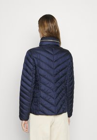 Marinblå pufferjacka med en chevron-quiltad design, hög krage med en kontrasterande rand och en slät, glänsande yta.