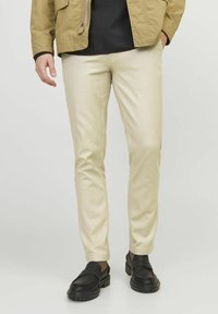 Beige Chinos mit Slim-Fit, aus glattem Stoff gefertigt, mit flachem Bund und subtilen Taschen, kombiniert mit schwarzen Slippern.