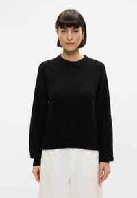 Black knitted sweater with a round neck, long sleeves, and a relaxed fit. Soft texture and even stitching throughout the garment.
