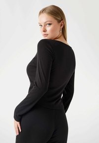 Black long-sleeve top with a fitted design and ribbed texture. Features a scooped neck and smooth seams for a sleek appearance.