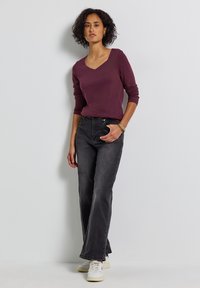 Burgundy V-ringad långärmad topp med tajta ärmar, kombinerad med hög midja, mörkgrå vida jeans och vita sneakers.