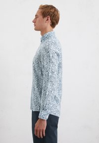 Camicia azzurra chiara con motivo floreale, maniche lunghe e colletto, abbinata a pantaloni blu scuro.