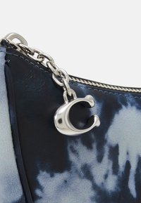 Sac en cuir bleu foncé avec un motif tie-dye, une chaîne en argent et un détail en forme de C près de la fermeture éclair.