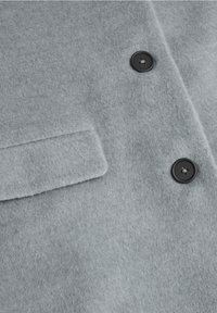 Šedý vlněný kabát s plstěnou texturou, jednou náprsní kapsou a dvěma černými knoflíky, který se vyznačuje čistým a jednoduchým designem.