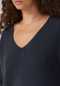 Donkerblauwe v-hals trui gemaakt van een gestructureerde stof, met een relaxte fit en subtiele stikdetails langs het midden.