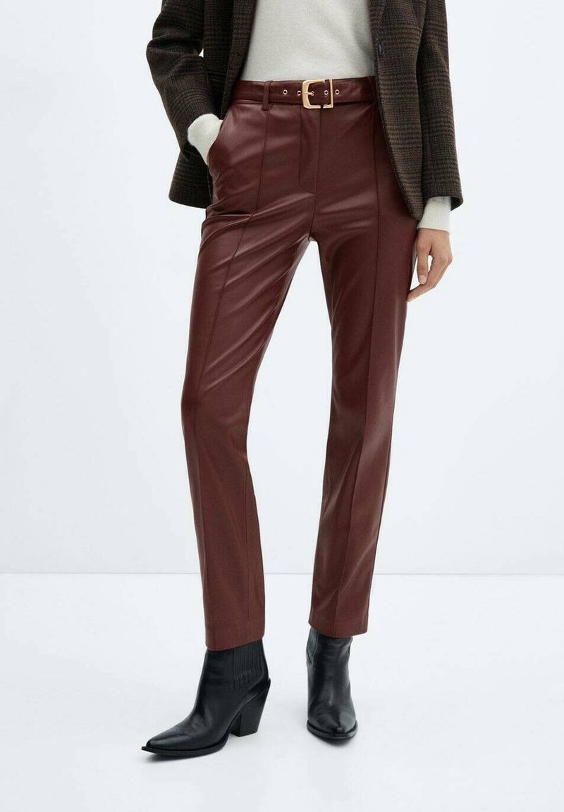 Femme portant un pantalon en cuir bordeaux taille haute avec ceinture, bottines noires à talons, pull blanc et blazer à carreaux foncé.