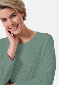 Hellgrüner, strukturierter Langarmpullover mit lockerer Passform und weitem Halsausschnitt, der ein dezentes Muster und gerippte Bündchen aufweist.