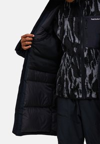 Svart och gråmönstrad fleecejacka med zip framtill, synlig innersulans isolering och en ficka på vänster bröst. Texturerad tygfinish.