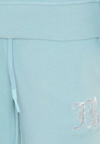 Pantalon de jogging bleu clair avec une texture douce, taille côtelée, cordon de serrage et un logo brodé blanc sur la jambe inférieure.