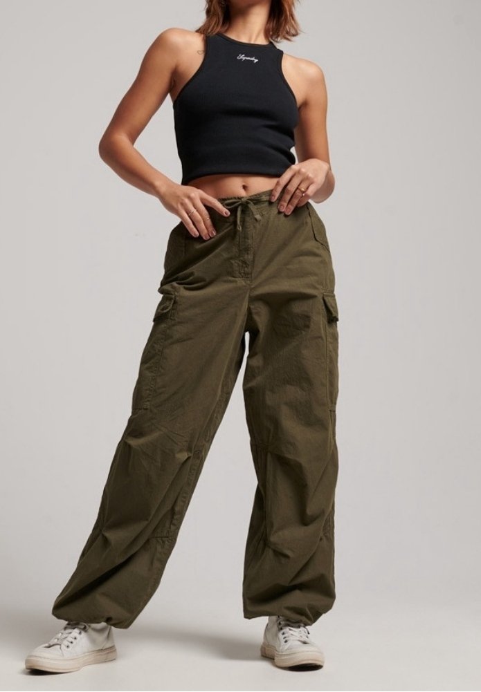 Zwarte geribbelde cropped top met logo, gecombineerd met losse, olijfgroene cargobroek. Witte sneakers maken de outfit compleet.