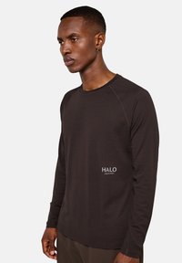 Langärmliges, strukturiertes Rundhals-Shirt in Dunkelbraun mit einem dezenten Logo auf der linken Seite und kontrastierenden Nähten entlang der Nähte.