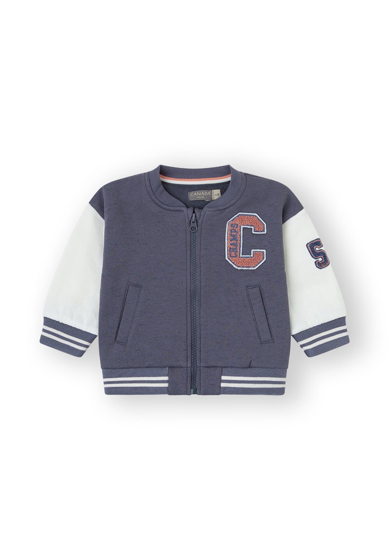 Chaqueta bomber de navy con cremallera y mangas blancas, puños a rayas y parches. Material suave, dos bolsillos frontales, cuello y dobladillo acanalados.