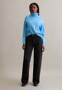 Hellblaues Rollkragensweater aus weichem Strickstoff, kombiniert mit hoch taillierten schwarzen weit geschnittenen Hosen und schwarzen Stiefeletten.