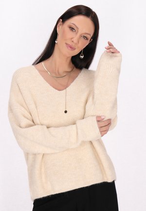 Beige, gebreide trui met een V-hals en lange, losse mouwen. Heeft een zachte, geribbelde textuur en een ontspannen pasvorm.