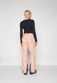 Pink ski pants with grey accents, elastic waistband, and zipped side openings. Worn with a fitted long-sleeve black top.