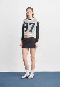 Witte mesh crop top met zwarte lange mouwen en het nummer "97", gecombineerd met een zwarte mini rok, witte scalloped sokken en zilveren schoenen.