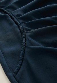 Marinblått tyg med detaljerad samlad textur, som har elastiska sömmar längs kanten, vilket framhäver en mjuk och slät fall.