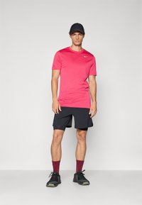 Czerwony t-shirt sportowy z krótkim rękawem i logiem Nike, zestawiony z czarnymi szortami. Uzupełniony burgundowymi skarpetkami i czarnymi butami sportowymi.
