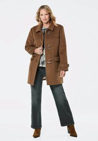 Brauner Woll-Dufflecoat mit Toggle-Verschlüssen, Brust- und Seitentaschen, kombiniert mit dunklen, leicht ausgestellten Jeans und braunen Wildleder-Stiefeletten.