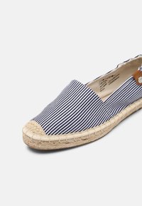 Chaussure slip-on en tissu rayé avec un bout rond, dotée d'une semelle en jute et d'un accent en cuir marron près de l'ouverture.