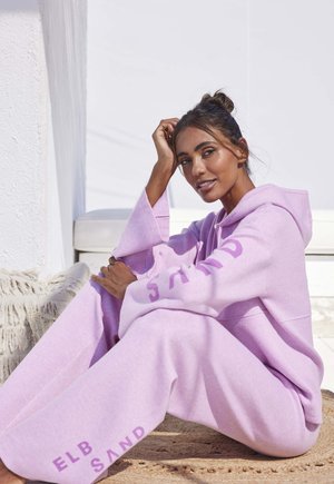 Helle lila oversized Kapuzenpullover und passende Jogginghose aus weichem Stoff, mit dem Text "ELB SAND" auf den Ärmeln und der Hose.