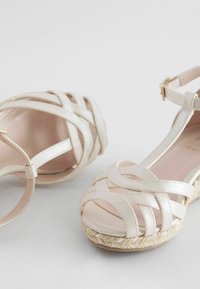 Stövlar med remmar i off-white läder och en vävd jute-sula. Har korsade remmar och en justerbar vristrem.