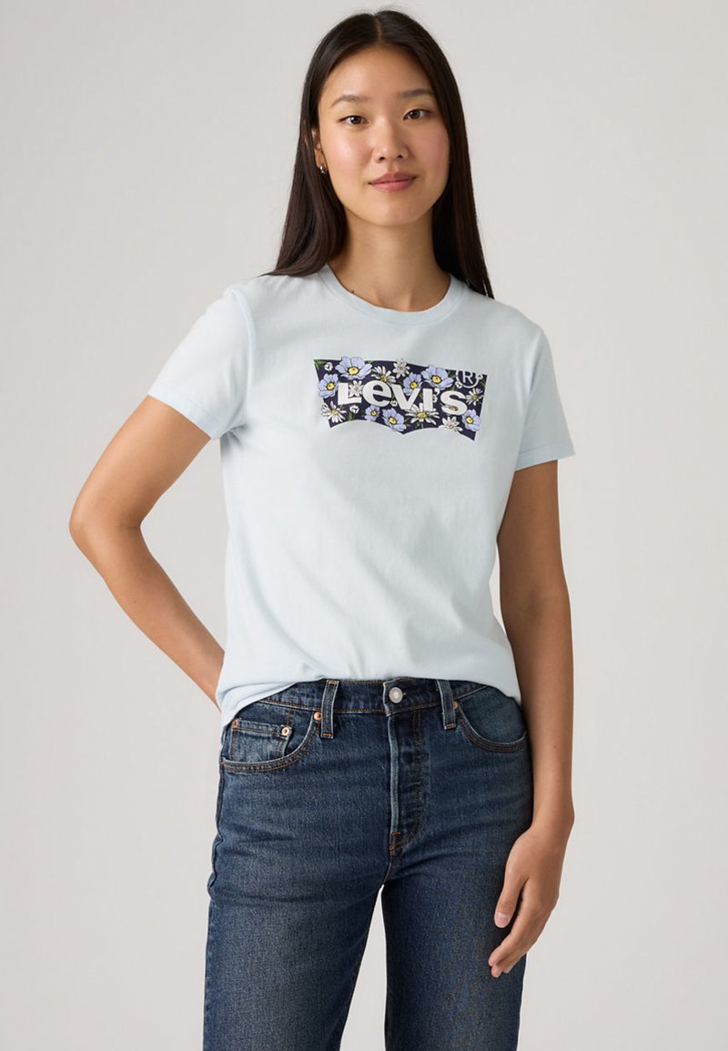 Ανοιχτό μπλε βαμβακερό t-shirt με γραφικό λογότυπο Levi's με λουλούδια μπροστά, συνδυασμένο με σκούρο τζιν παντελόνι. Κοντά μανίκια, σχέδιο με στρογγυλή λαιμόκοψη.