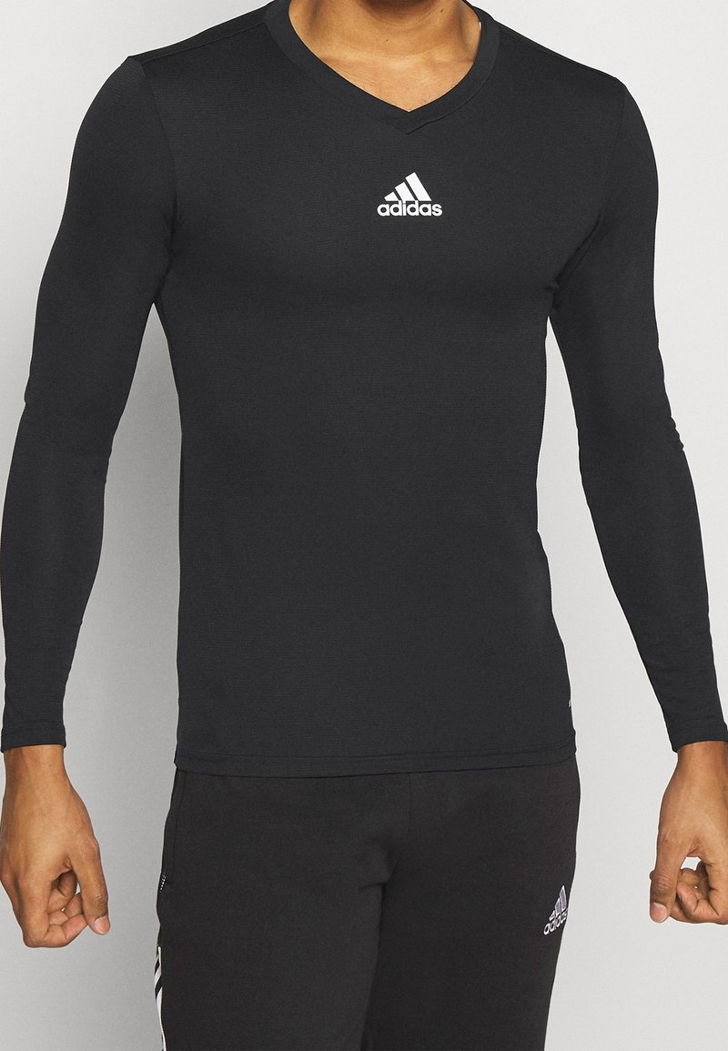 Schwarz langärmliges Sporthemd mit V-Ausschnitt, aus dehnbarem Material, mit einem weißen Adidas-Logo auf der Brust. Enganliegende Passform.