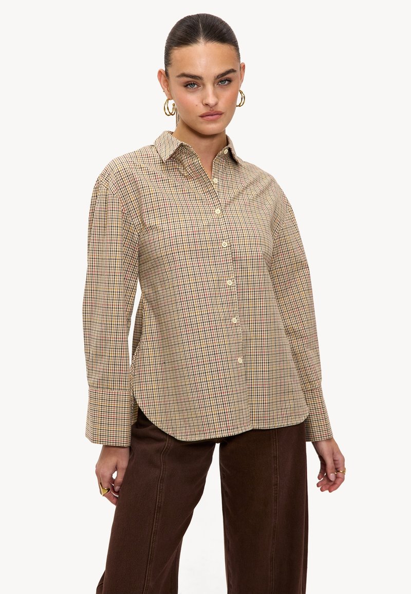Chemise à carreaux beige, marron et rouge. Dotée d'un col, de manches longues et d'une coupe décontractée. Tissu doux avec une texture lisse.