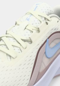 Αθλητικό παπούτσι Nike σε εκρού χρώμα με ανοικτά γαλάζιες λεπτομέρειες, επάνω μέρος από υφή διχτυού, λεπτά κορδόνια και μοβ διακοσμητικά στη σόλα.