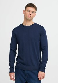 Marineblå strikket genser med lange ermer, rund hals, ribbede mansjetter og en jevn tekstur, kombinert med blå jeans.